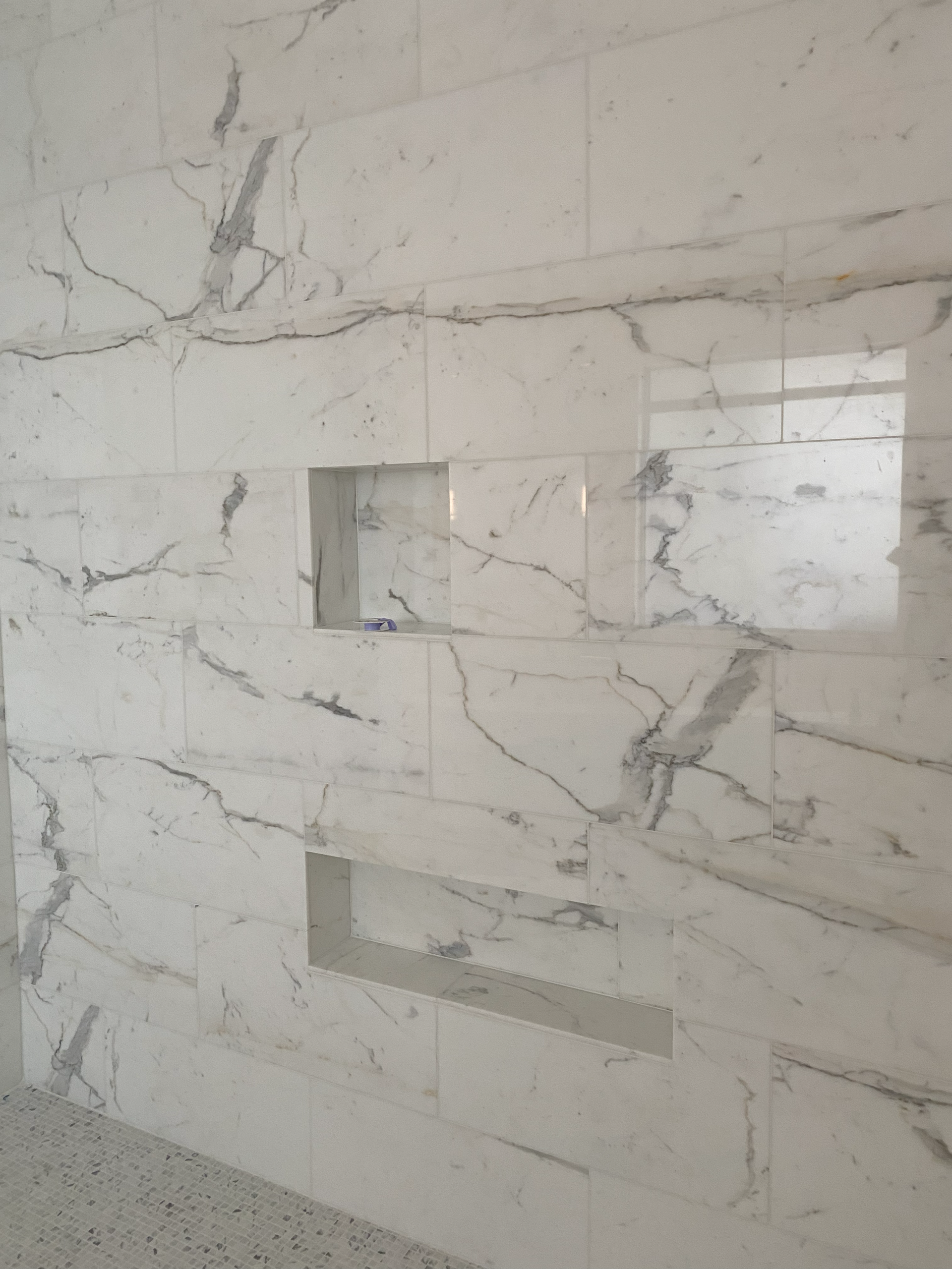 White marble tile shower wall with three built-in shelves.