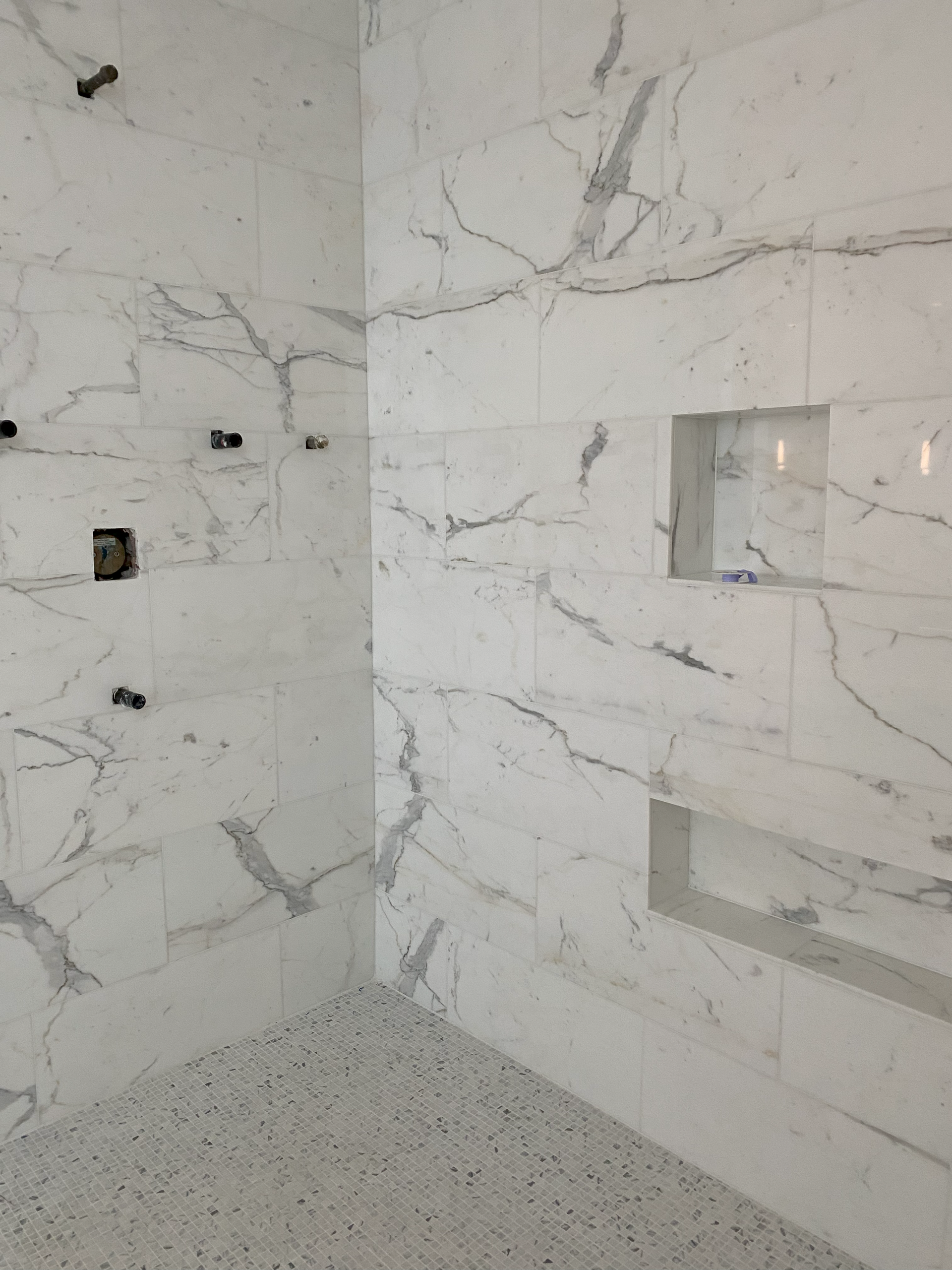 White marble-tiled shower with recessed shelves and a speckled floor.