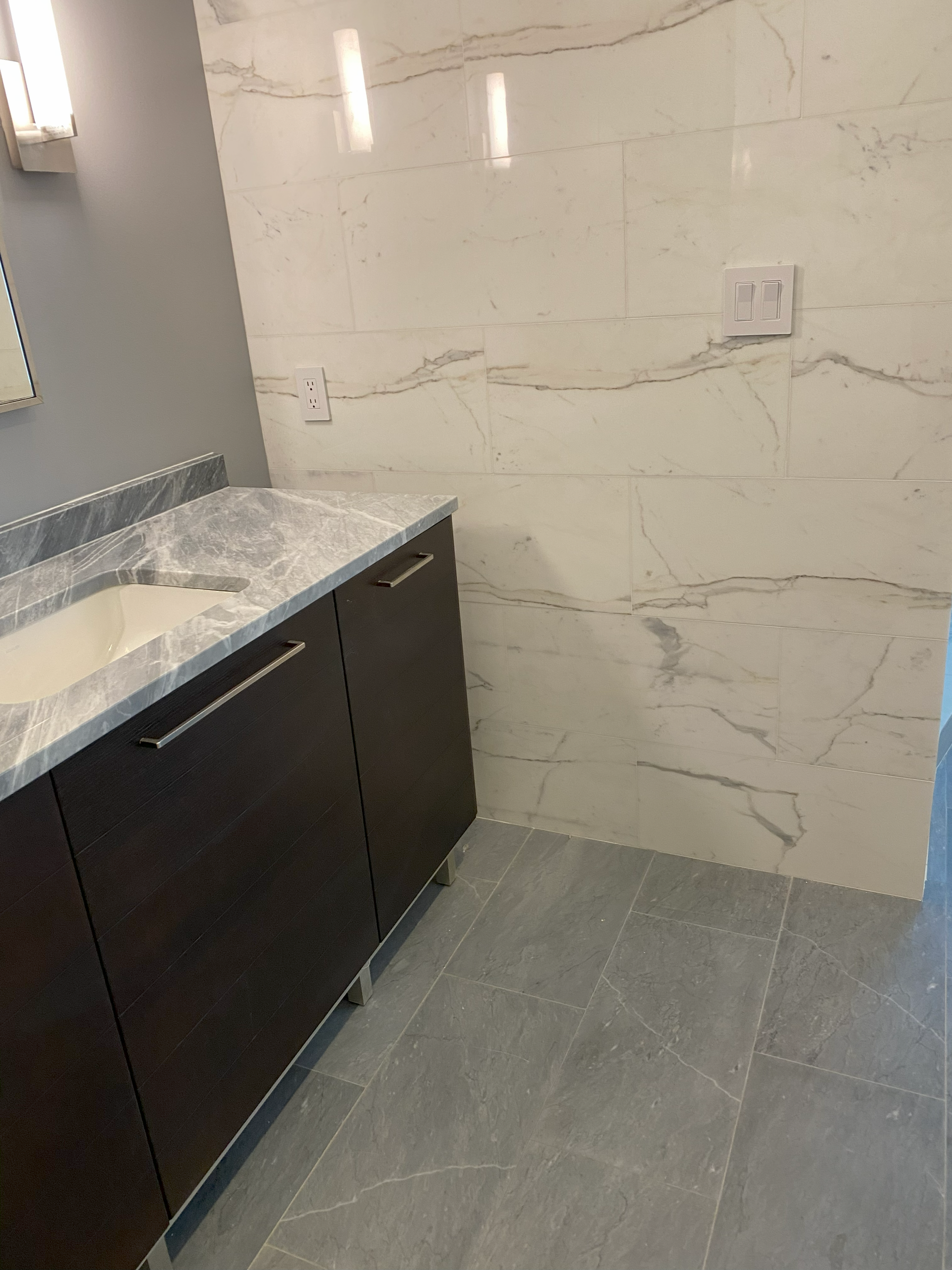 Bathroom with dark brown vanity, gray countertop, white marble tile wall, and gray floor.
