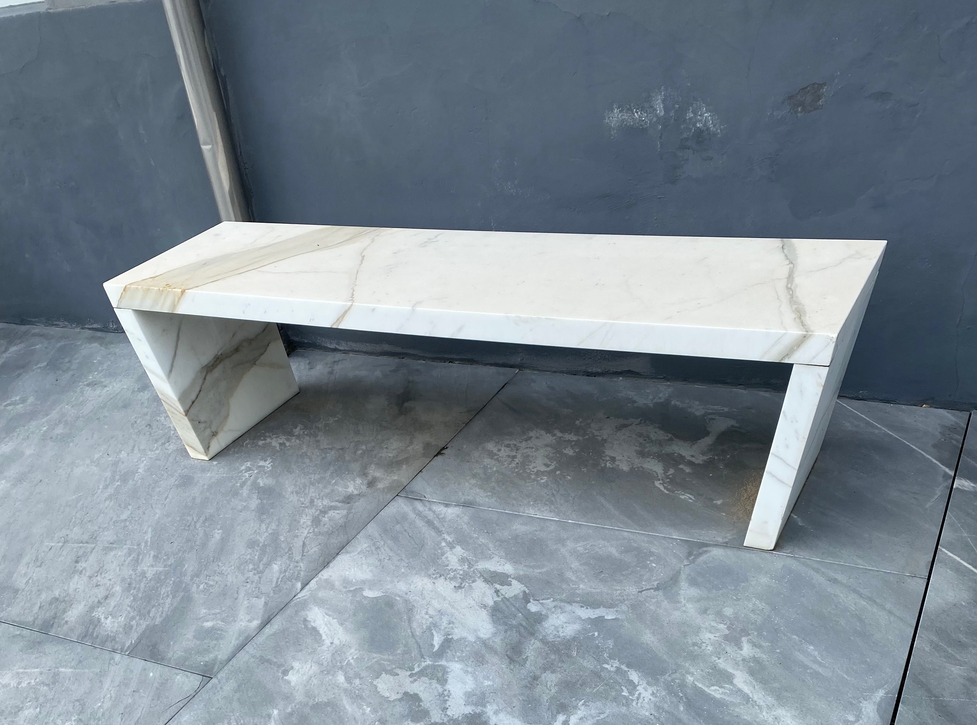 Marble bench with beige and brown veining sits on gray tiled floor against a dark gray wall.