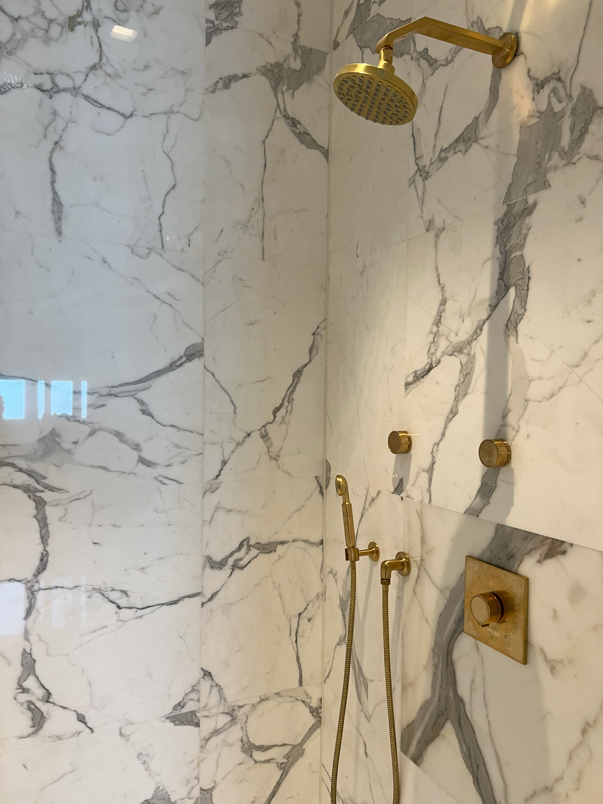 Gold shower fixtures against white and gray marble tiles in a bathroom.