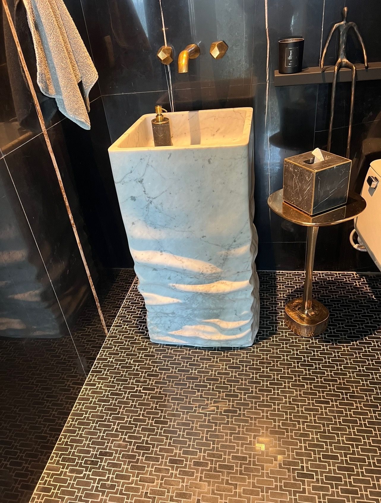 Bathroom with light blue, textured pedestal sink, gold fixtures, dark tiled floor.