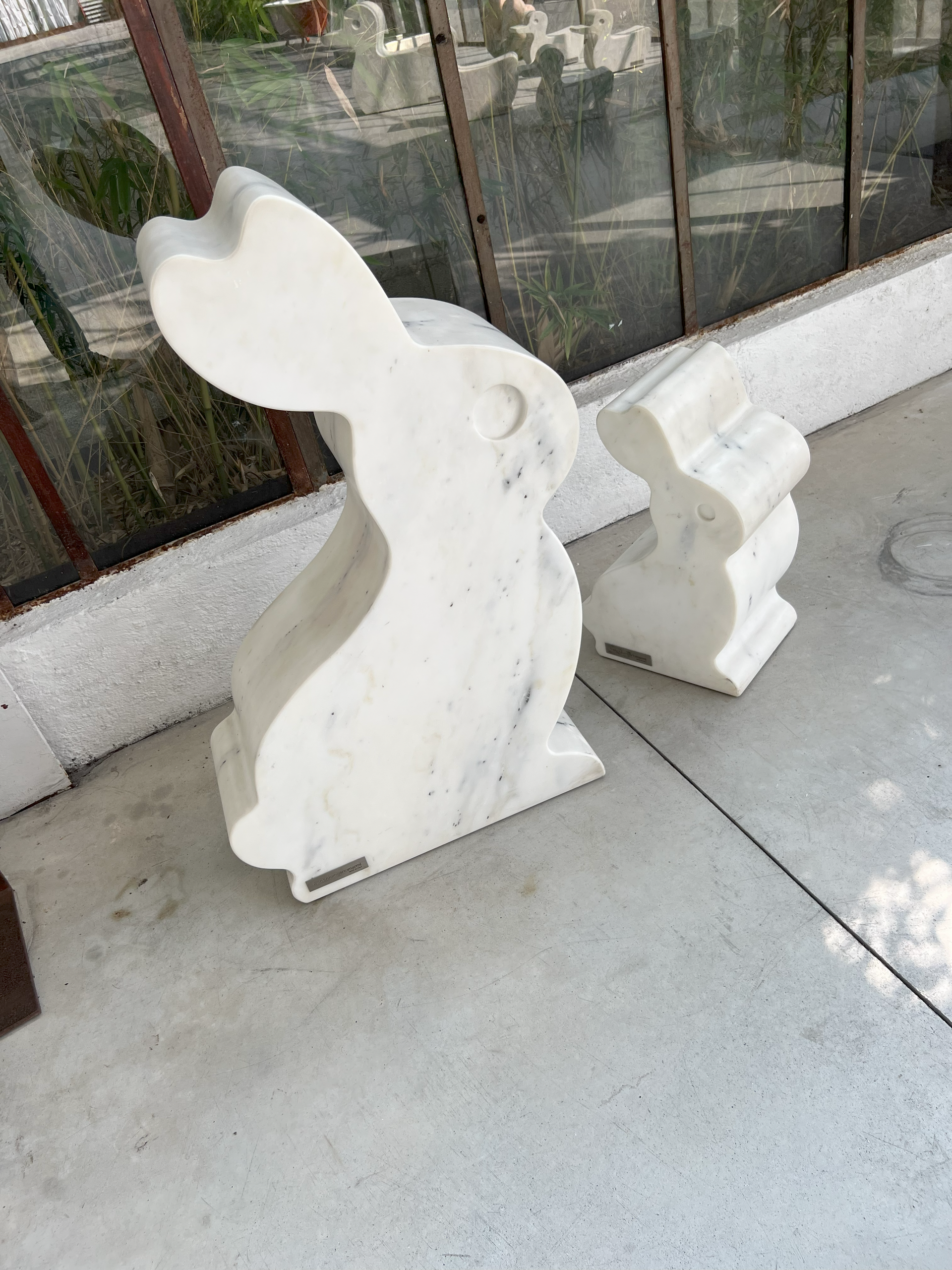 Two white marble rabbit sculptures outdoors. One upright, one seated.
