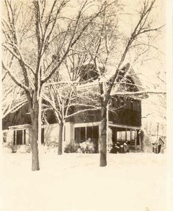 A snow-covered house with bare trees. White snow covers the yard and rooftops.
