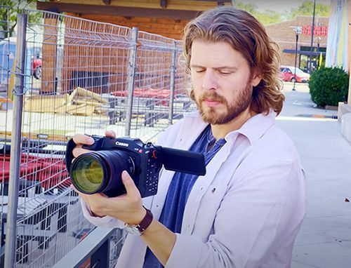 Man holding black Canon camera looking at the screen while shooting video.