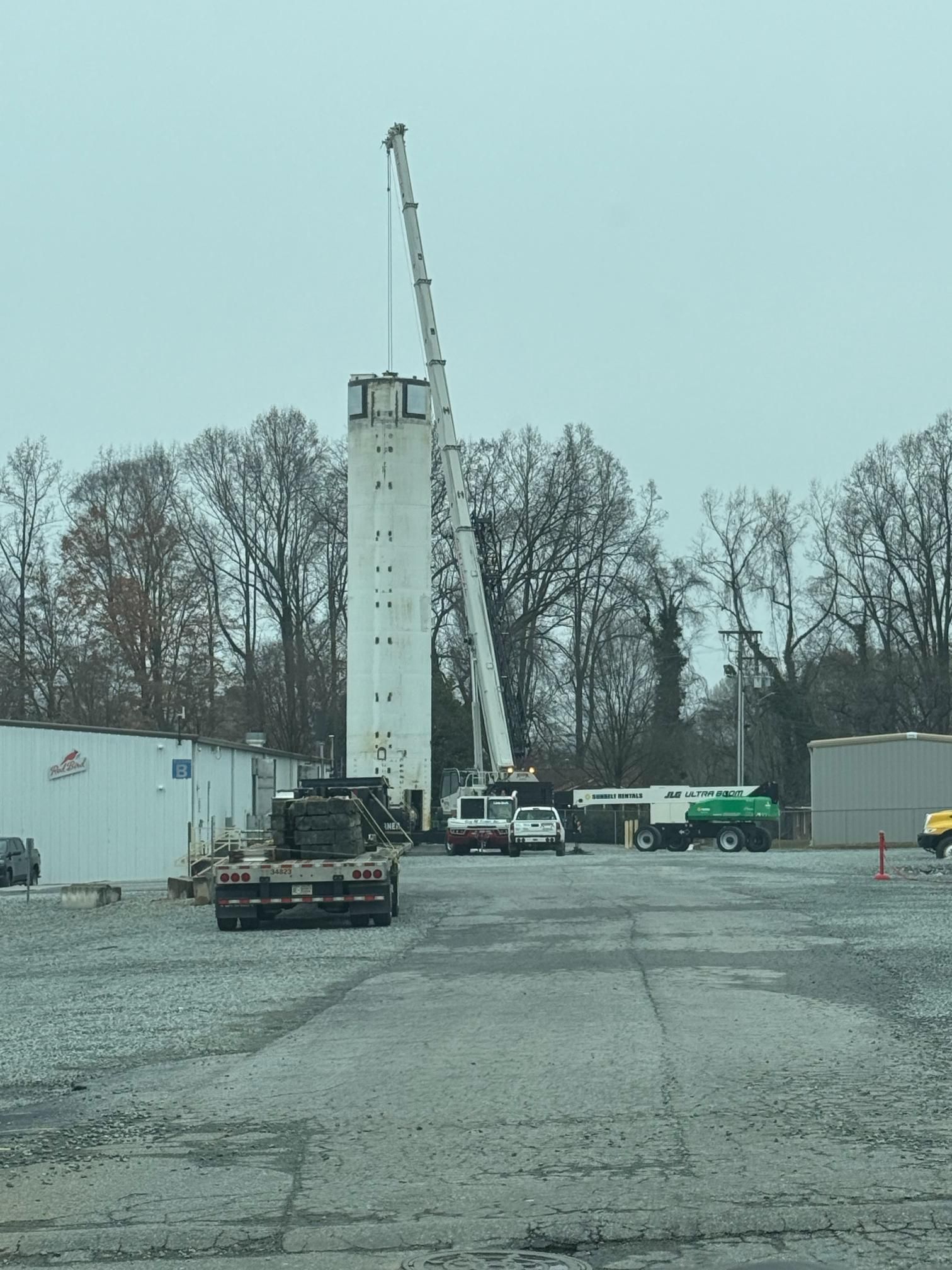 A tall white tower with a crane working on its top in an industrial setting. Overcast sky.