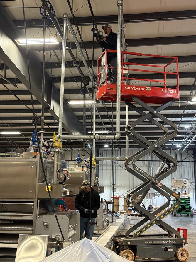 Person on a ladder working inside a garage with equipment including a welding torch and oxygen tank.