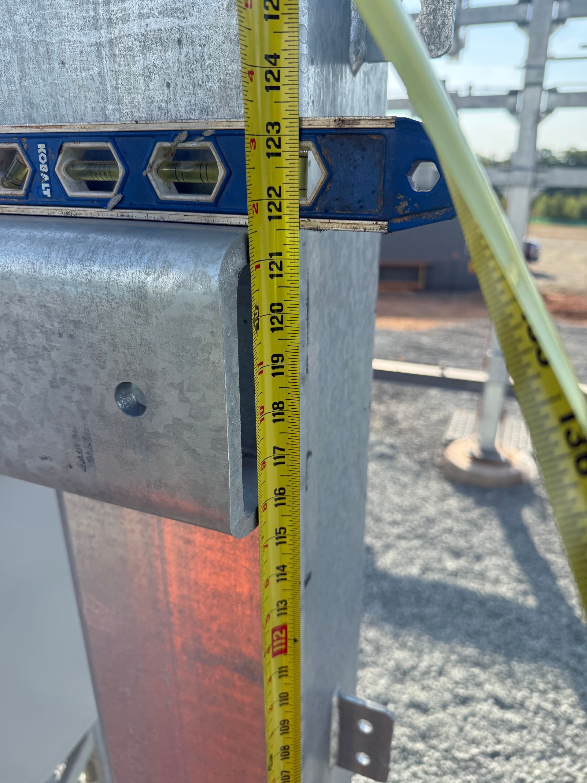 Tape measure against blue metal equipment outdoors on gravel.