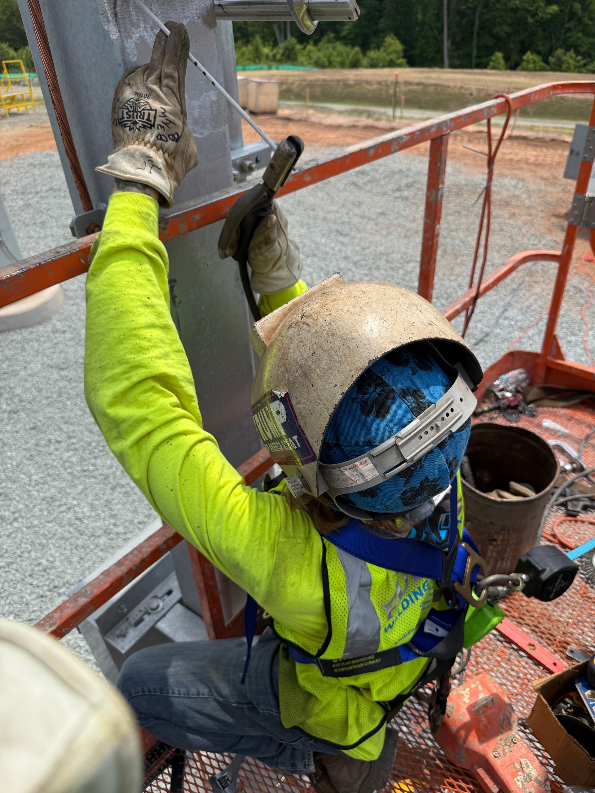 Worker in bright green gear and helmet climbing a red metal structure outdoors