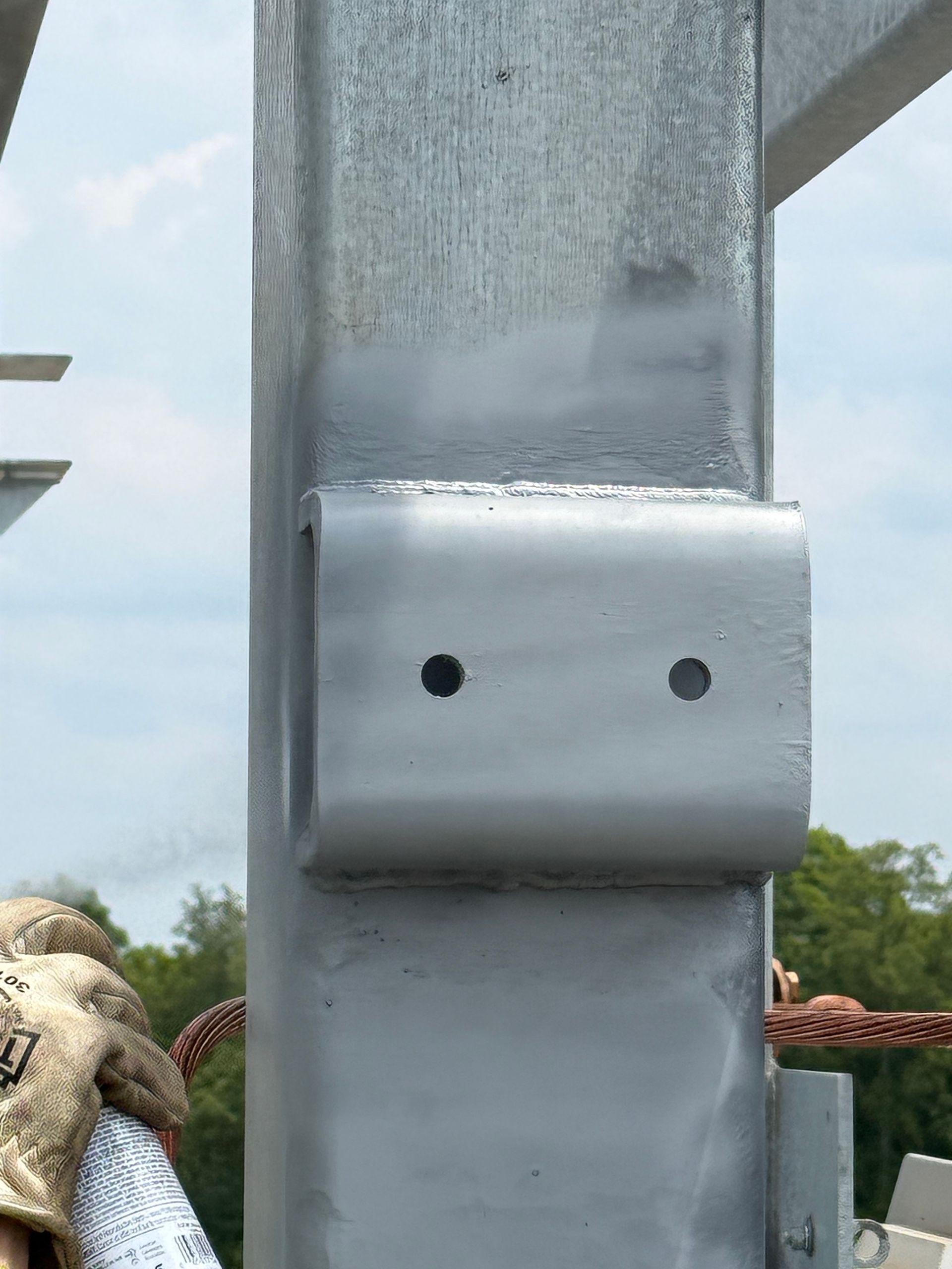 Close-up of a gray metal post with a bolted bracket and a rope barrier against a sky background