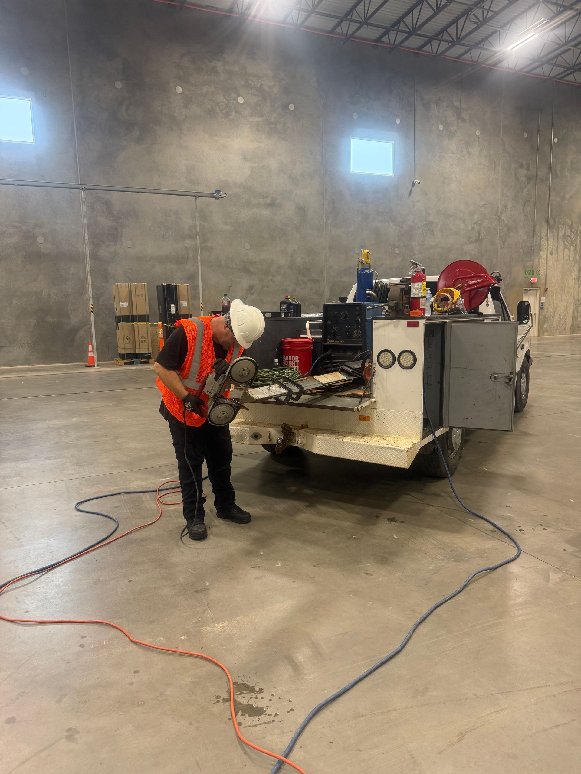 Worker in orange vest and hard hat operating machinery in a large industrial warehouse.
