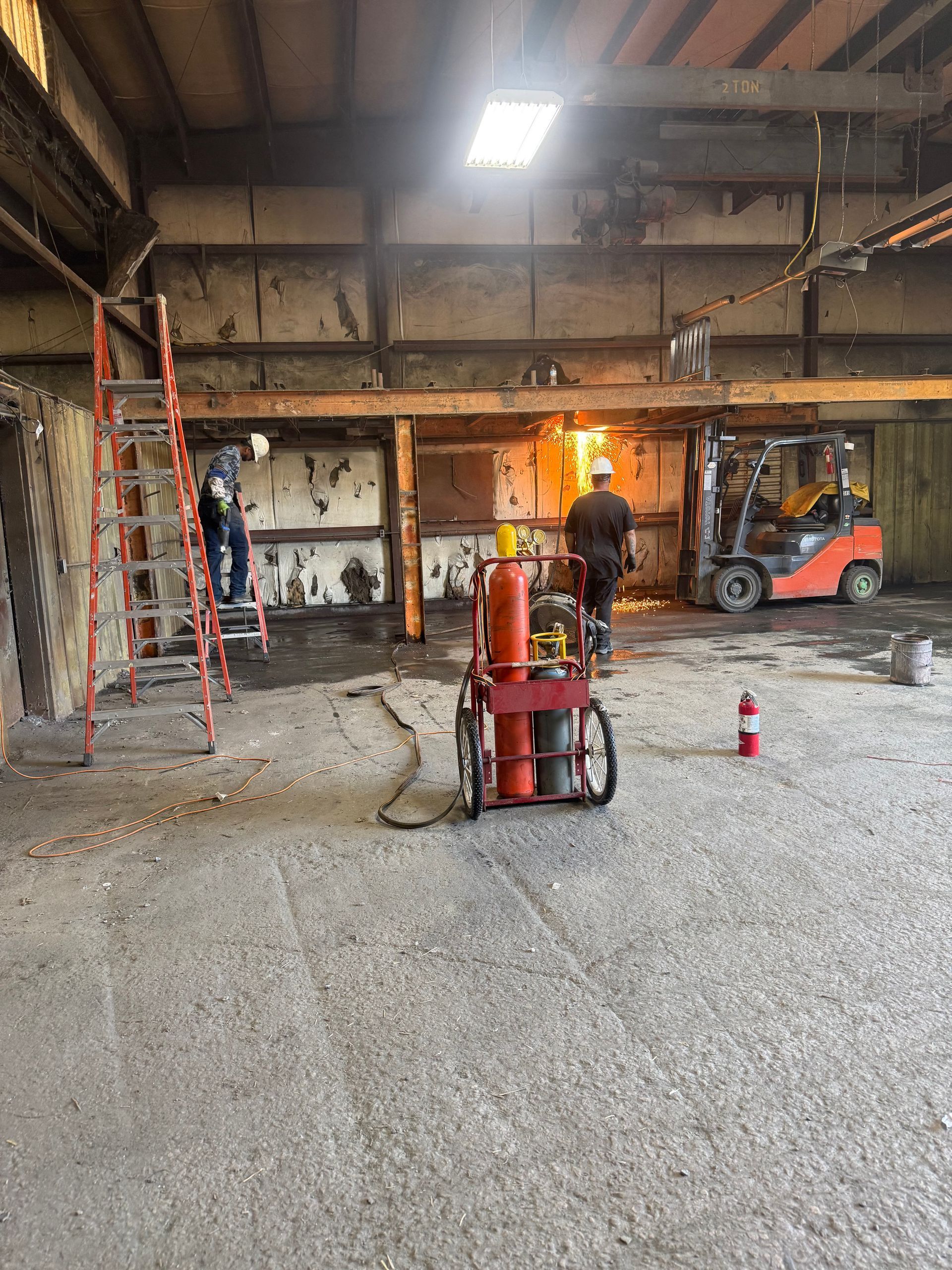 Construction site interior with forklift, worker, red ladder, and flames near a wall opening