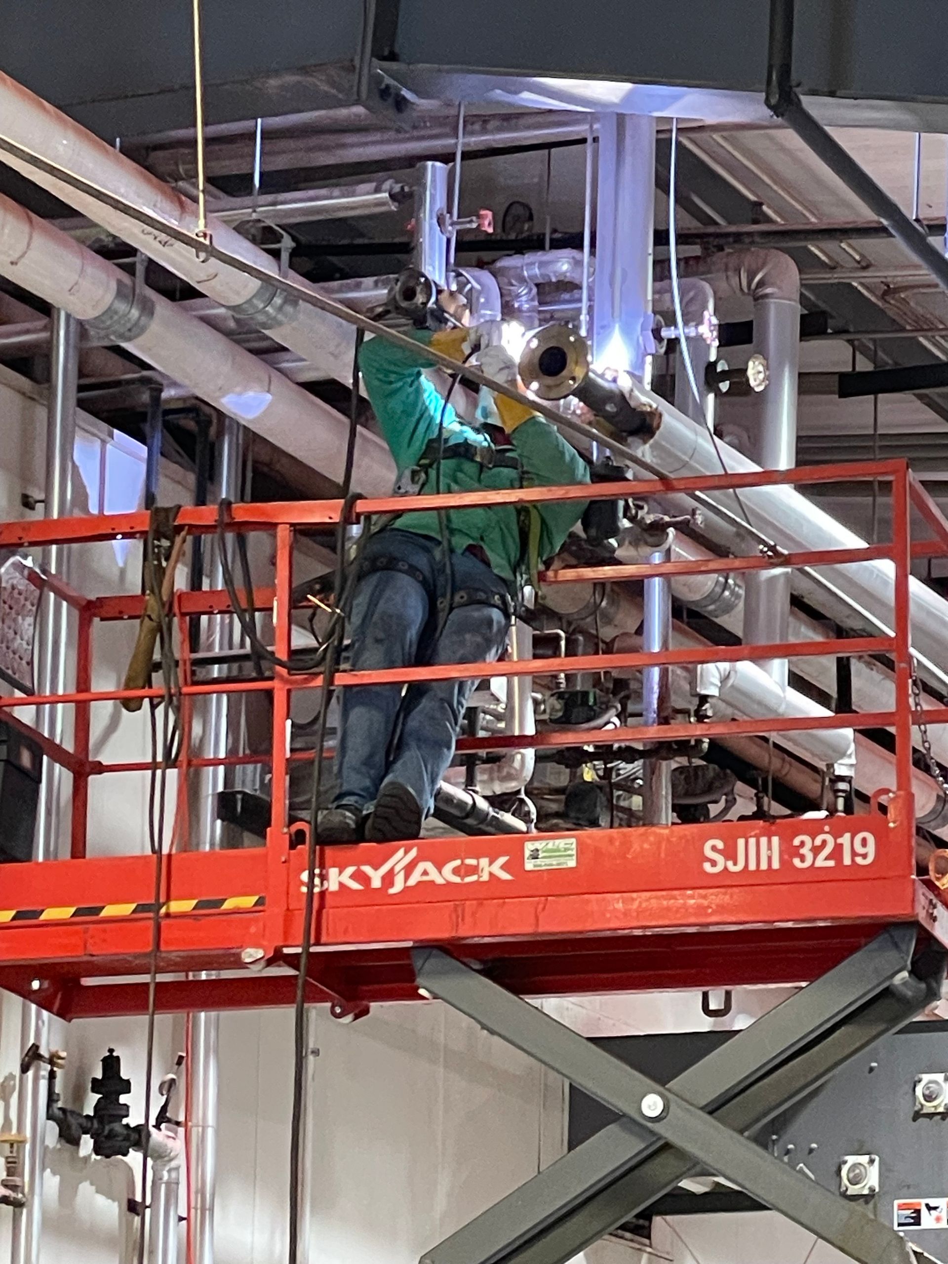 Welder using a torch on a metal pipe, wearing gloves and safety gear, creating a weld.
