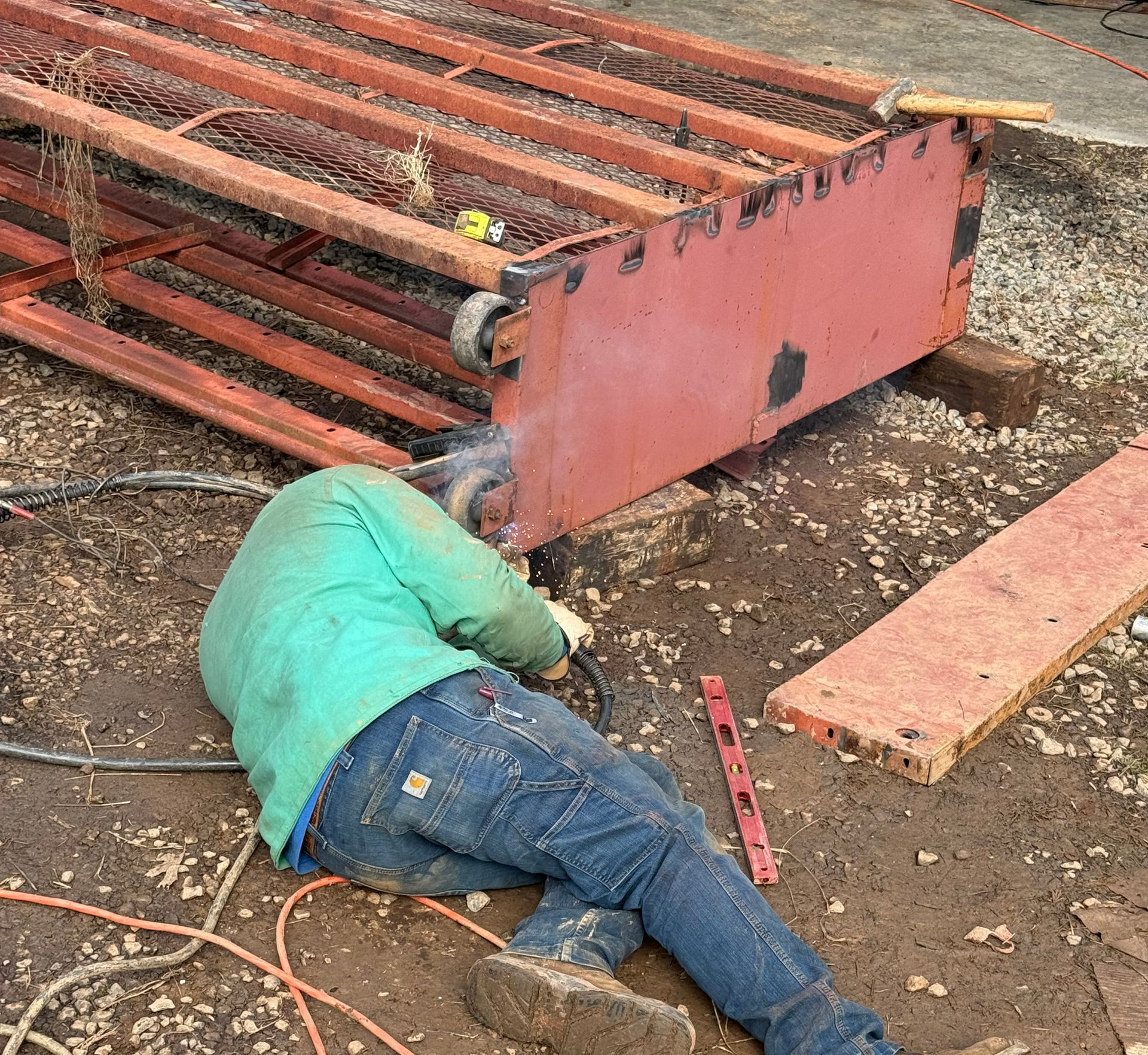 Worker lies beside a fallen red metal scaffold on muddy ground at a construction site.