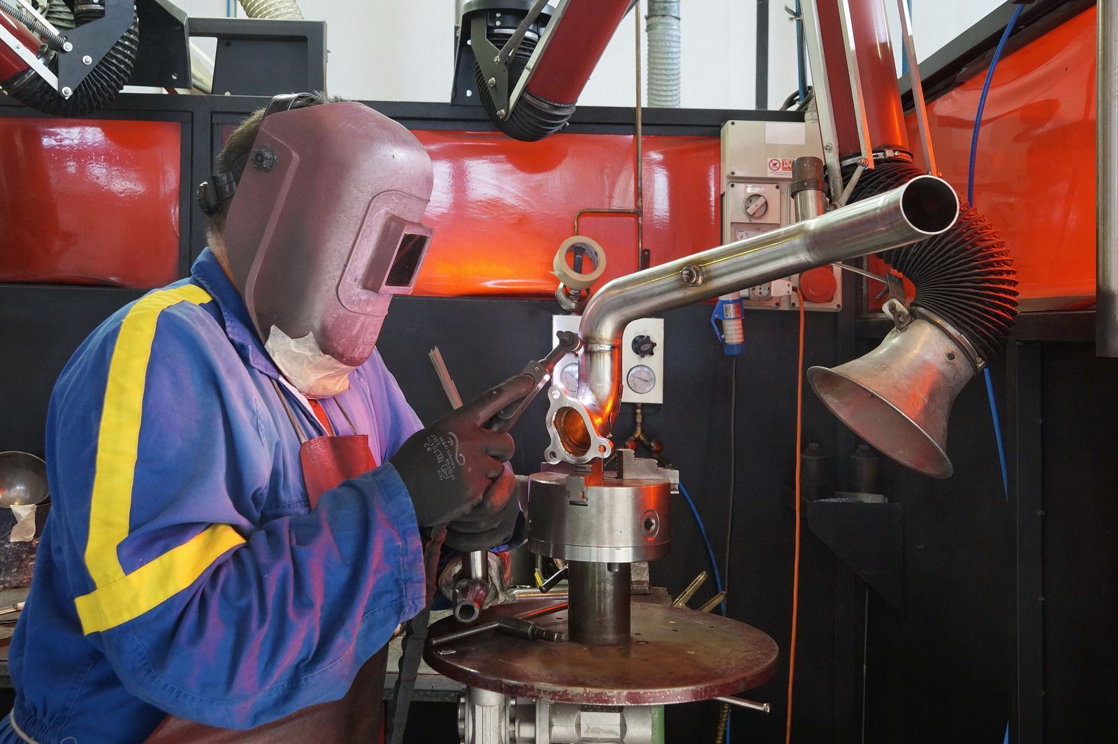 Welder wearing gloves using a welding torch on metal pipes. Sparks and bright light are present.