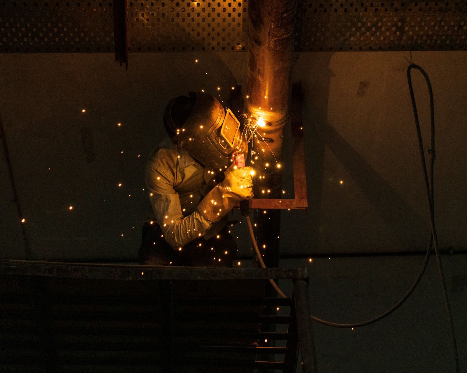 Welder using a torch on a metal pipe, wearing gloves and safety gear, creating a weld.
