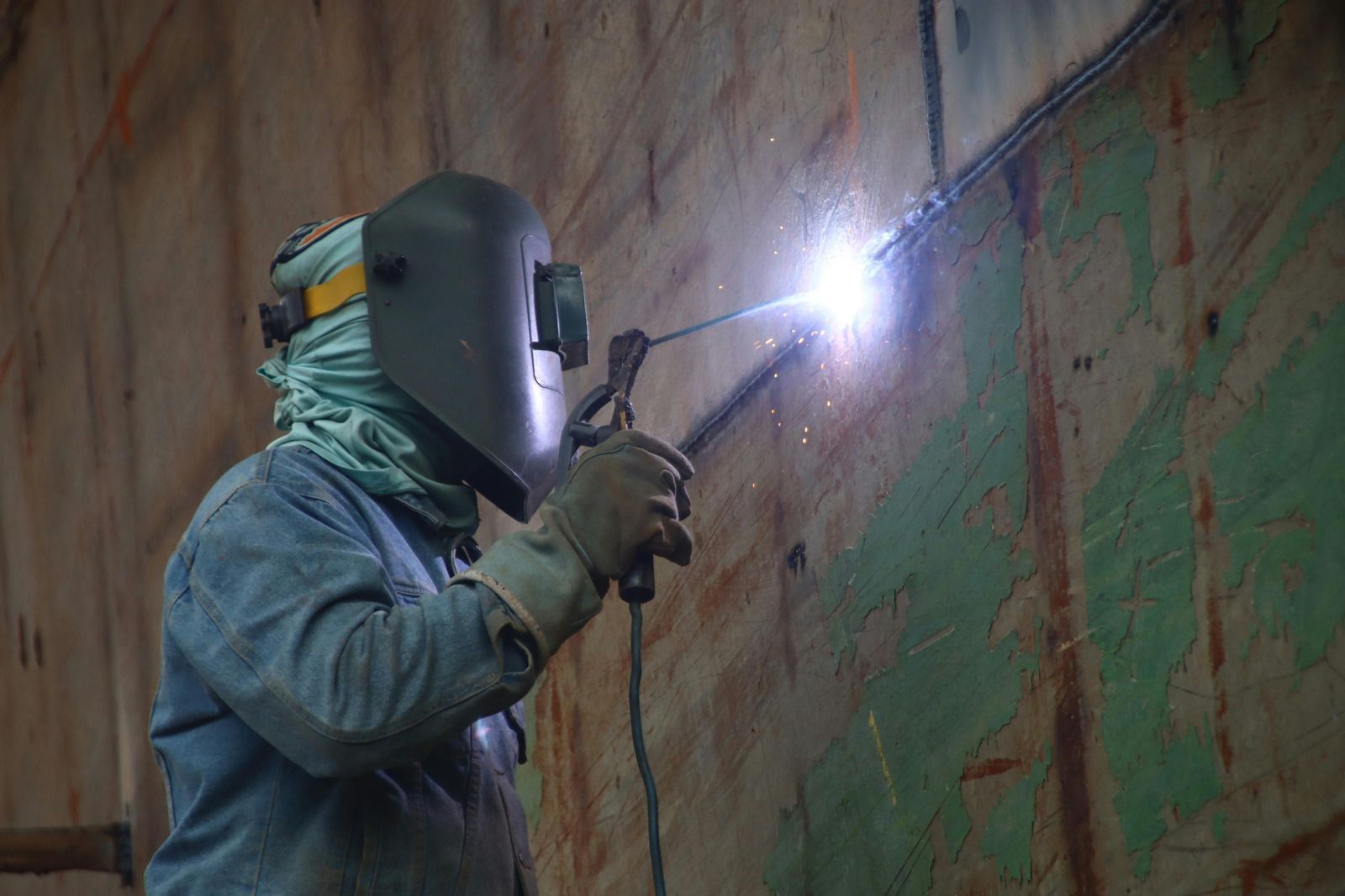 Welder wearing gloves using a welding torch on metal pipes. Sparks and bright light are present.
