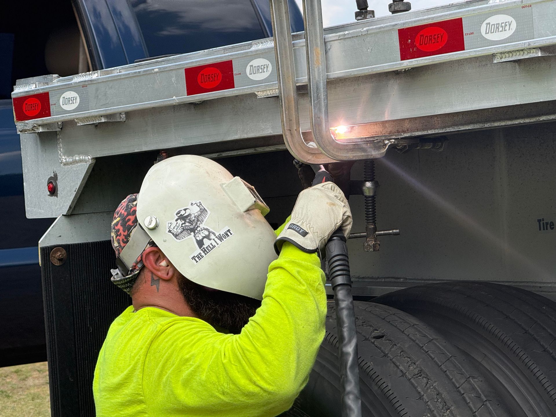 Worker in hard hat welding under a truck trailer wheel well