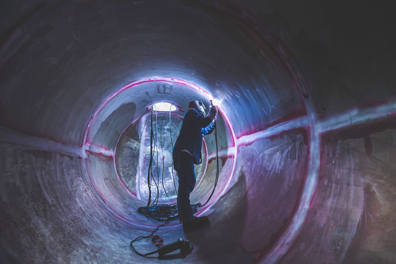 Welder using a torch on a metal pipe, wearing gloves and safety gear, creating a weld.