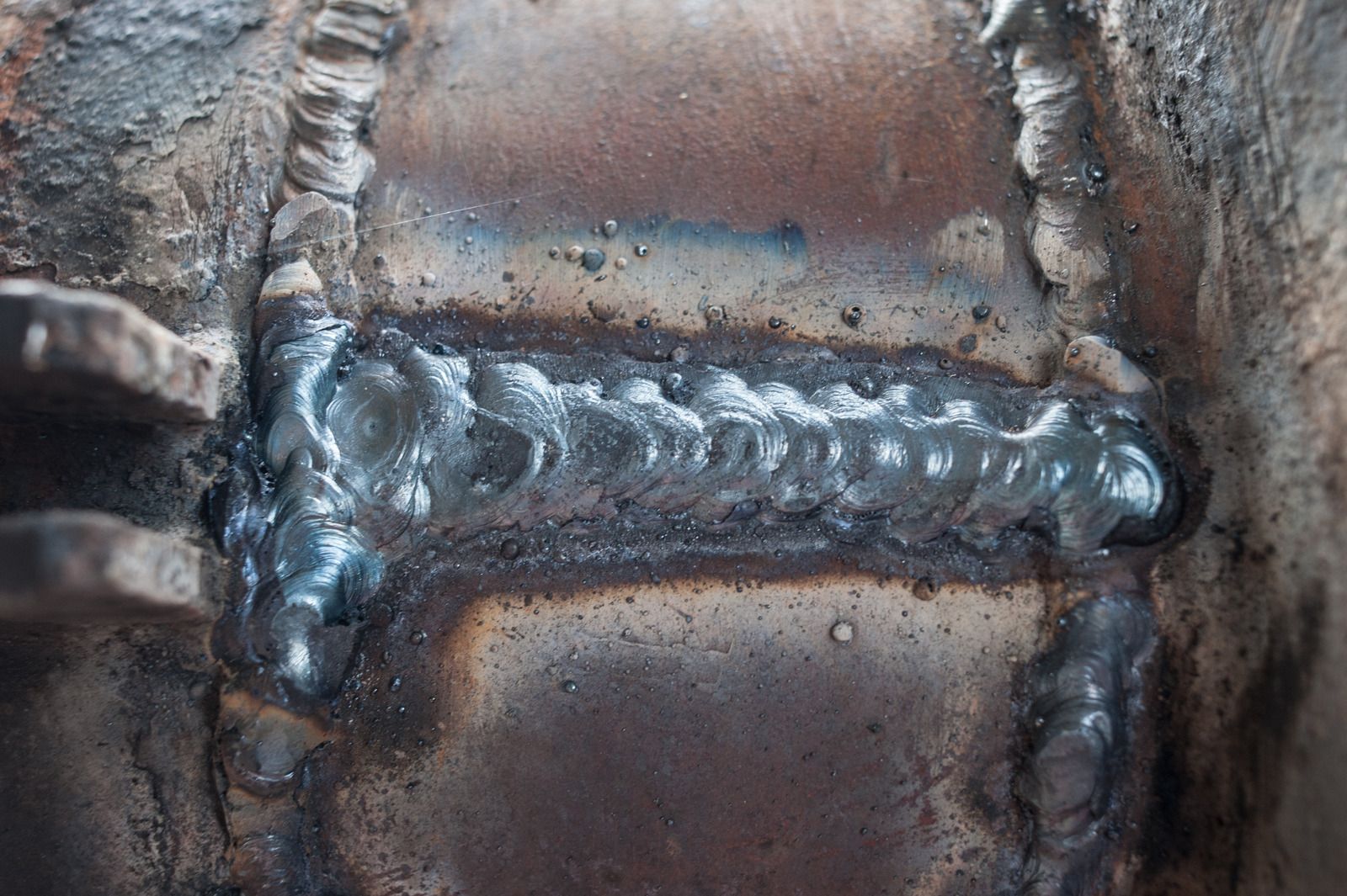 Welder wearing gloves using a welding torch on metal pipes. Sparks and bright light are present.