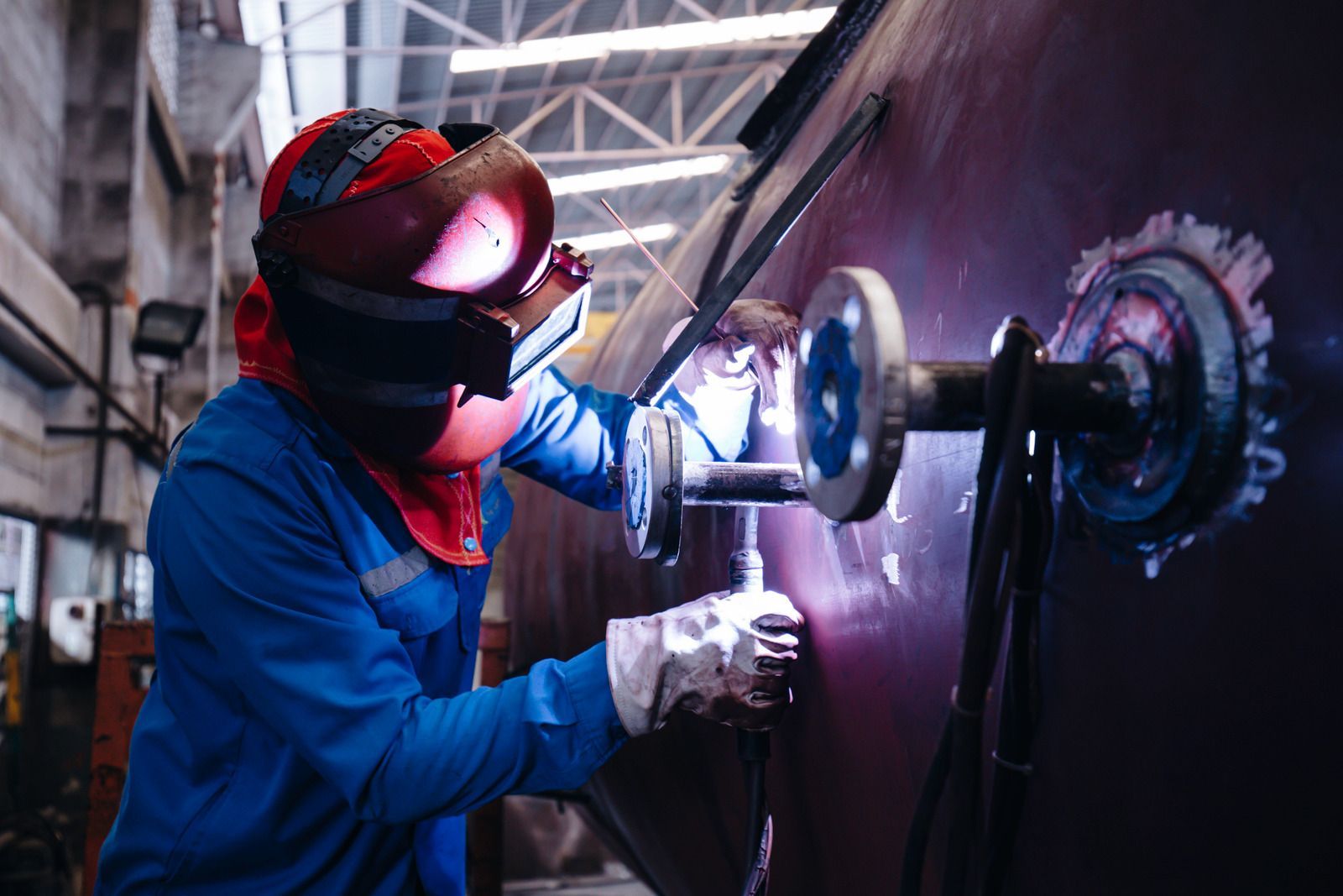 Welder using a torch on a metal pipe, wearing gloves and safety gear, creating a weld.
