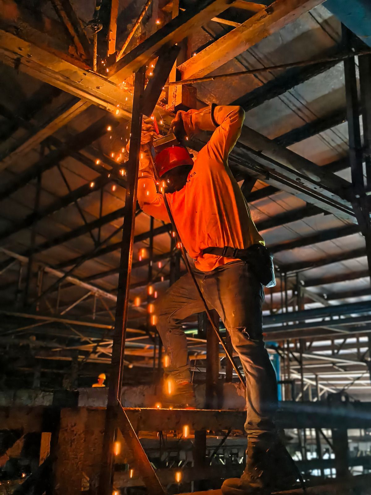Welder wearing gloves using a welding torch on metal pipes. Sparks and bright light are present.