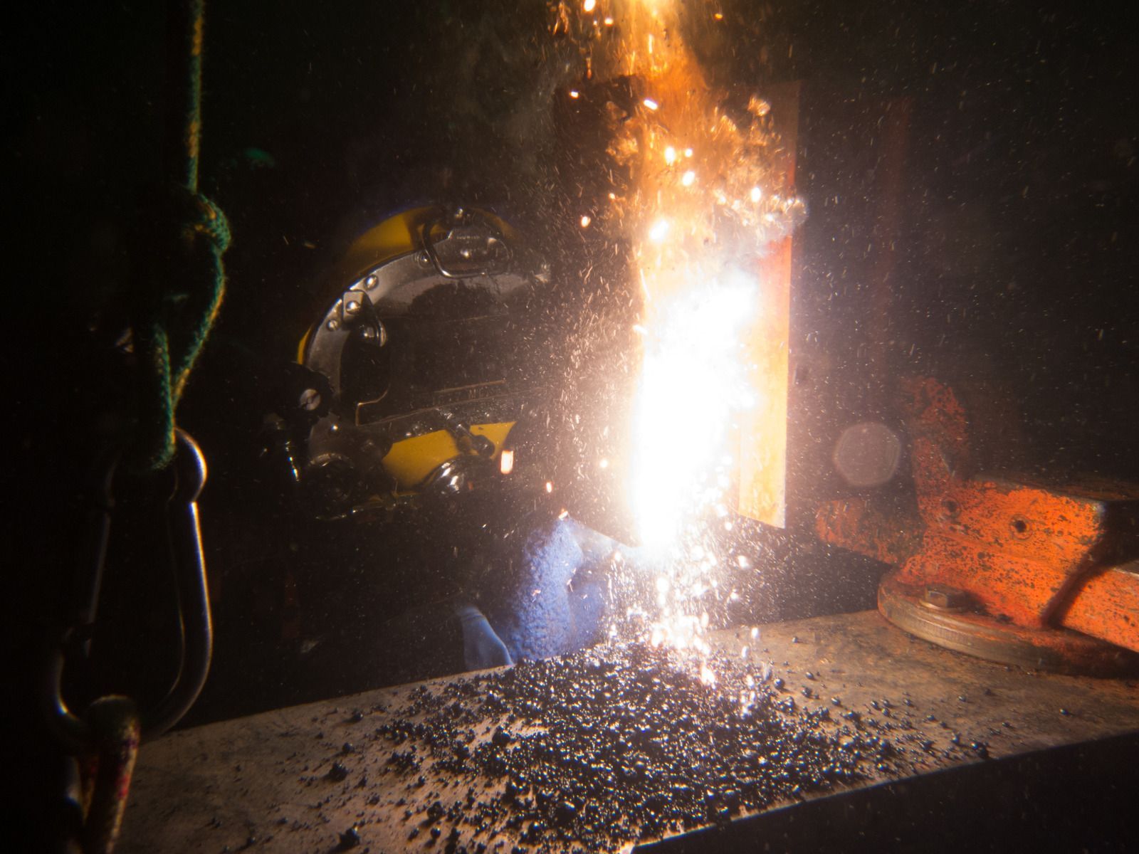 Welder using a torch on a metal pipe, wearing gloves and safety gear, creating a weld.