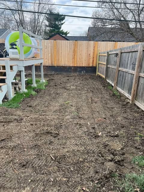 Backyard dirt strip beside wooden fences, with a white deck and green chair on the left.