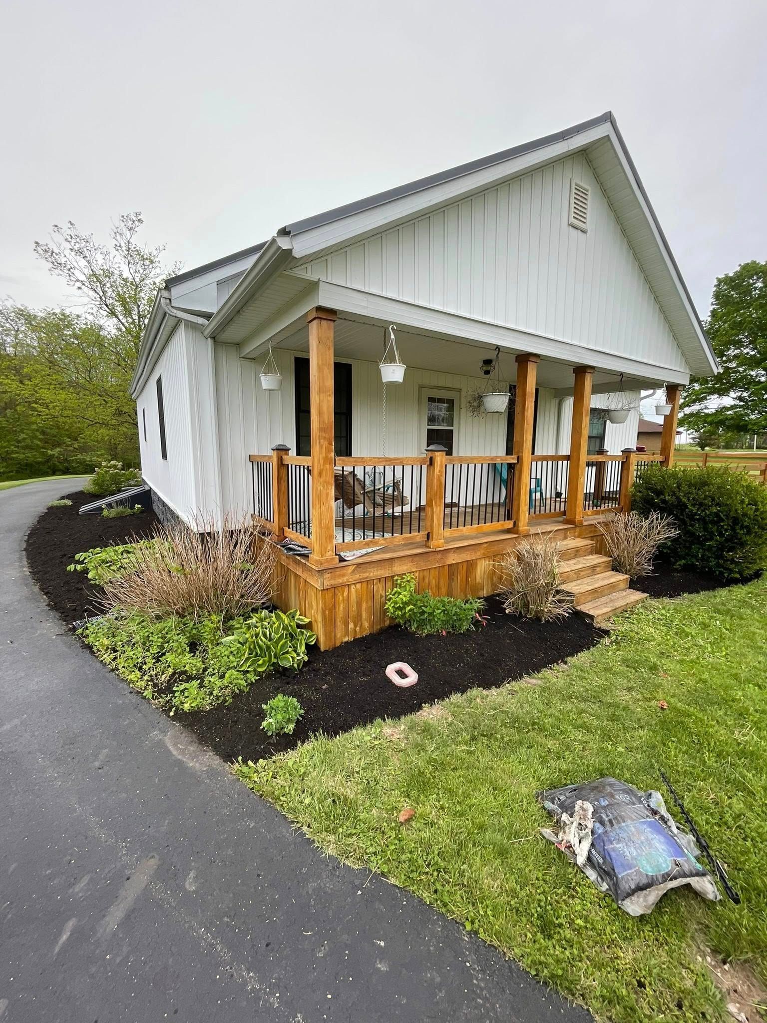 Small white house with a wooden porch, surrounded by landscaped shrubs and a curved paved walkway.