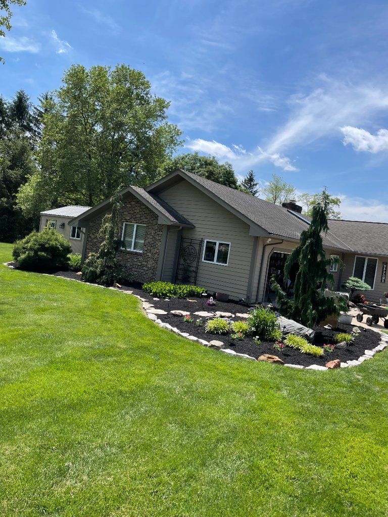 Small gray house with a landscaped flower bed and green lawn under a blue sky.
