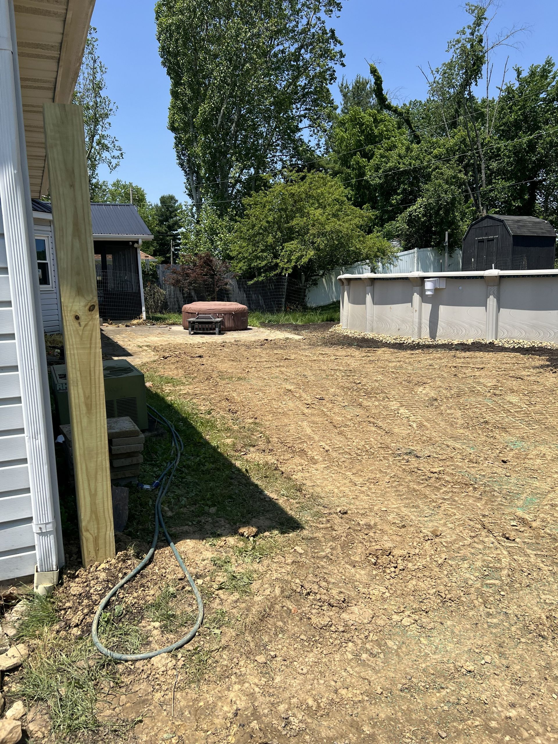 Backyard with dry grass, trees, and a small brick fire pit beside a house and shed