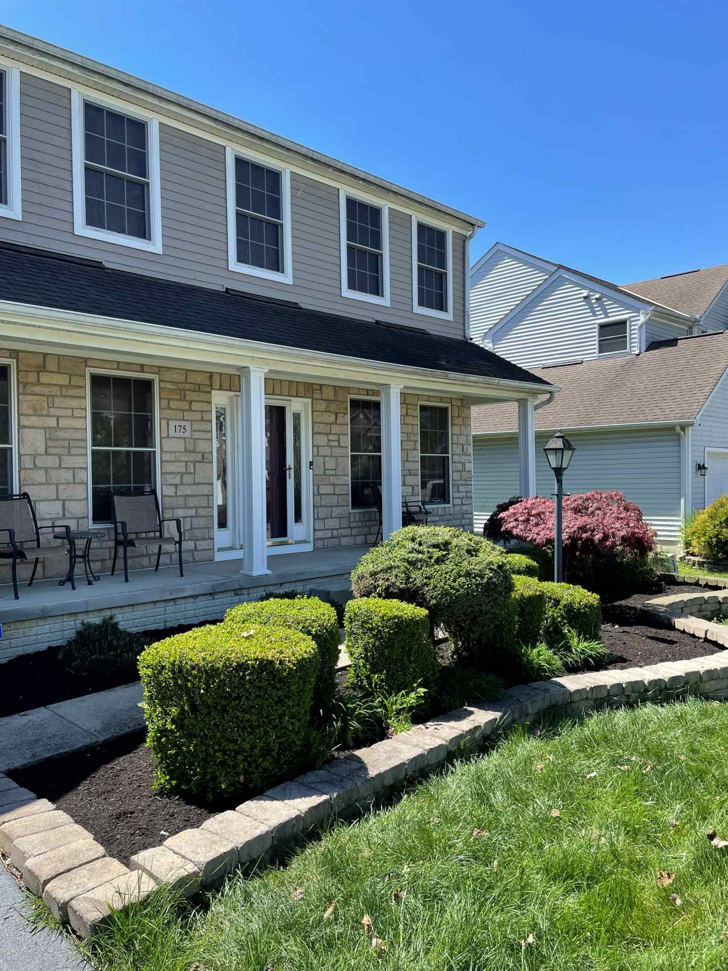 Two-story suburban house with a front porch, trimmed shrubs, and a manicured lawn