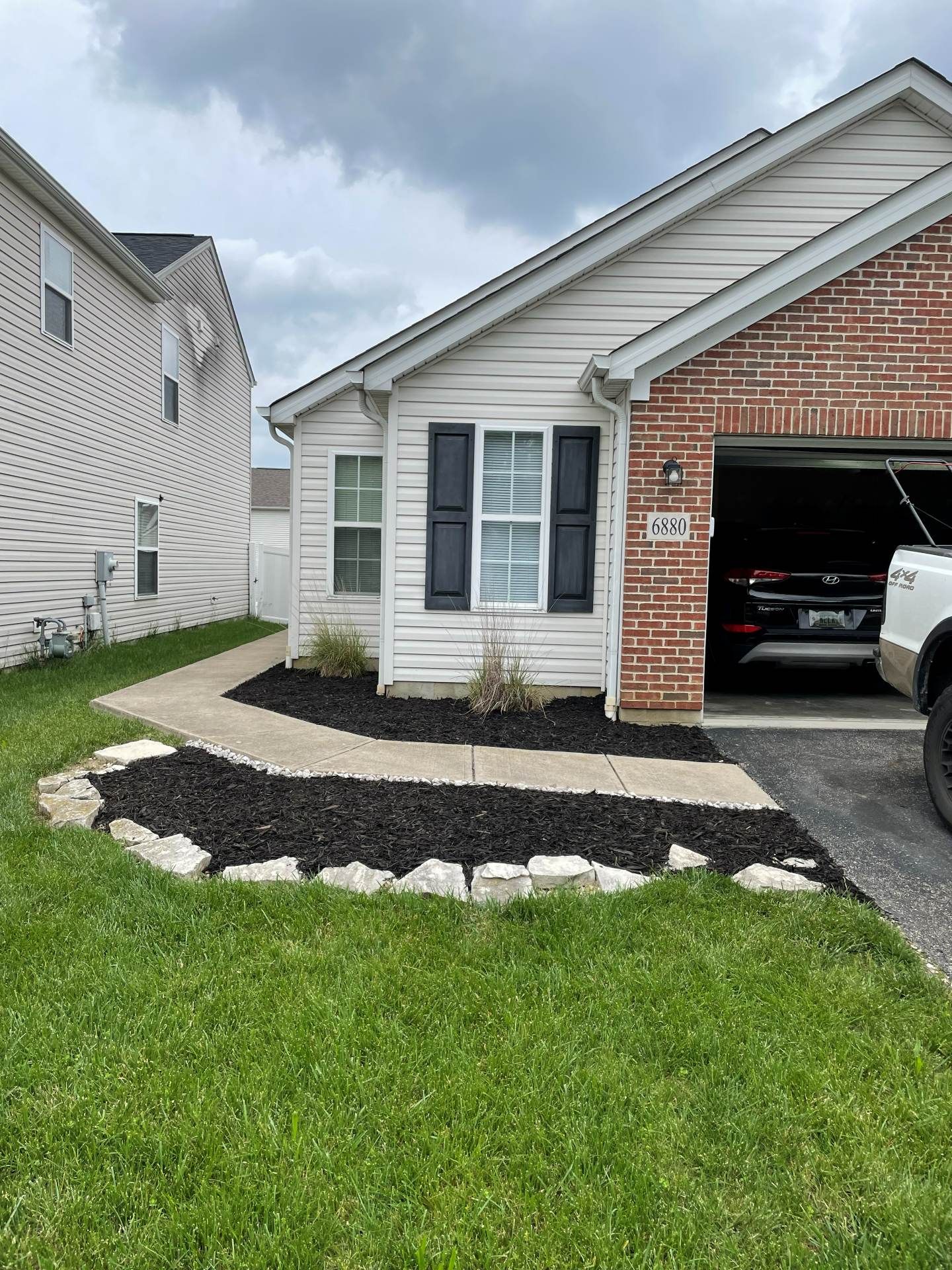 Front yard with a black mulch bed, white stones, and a brick garage with an open door.