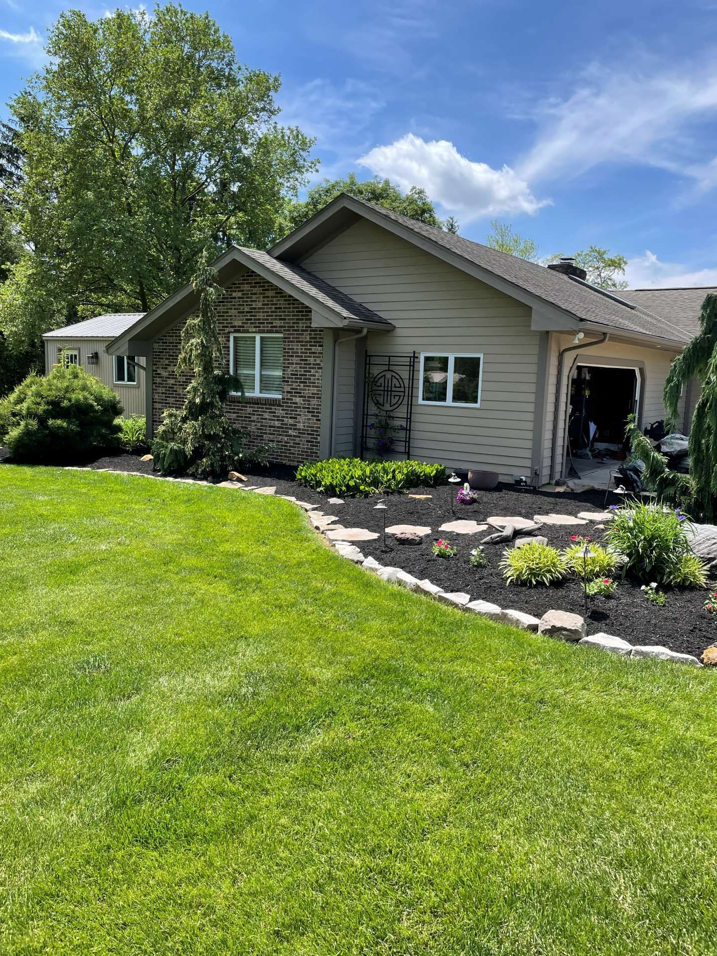 Single-story house with gray siding, green lawn, and landscaped front yard on a sunny day