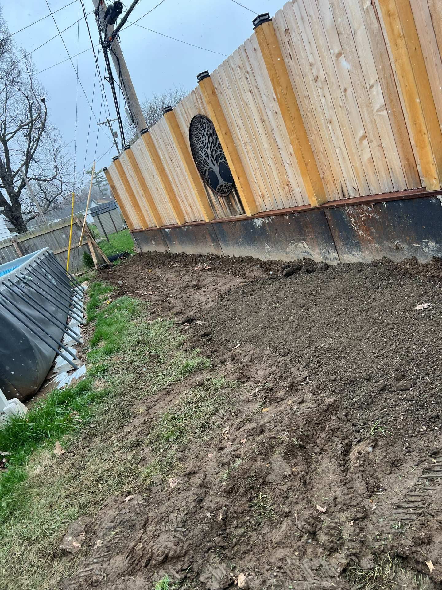 Muddy dirt path beside a yellow fence with a dark patch and a chain-link fence along the left