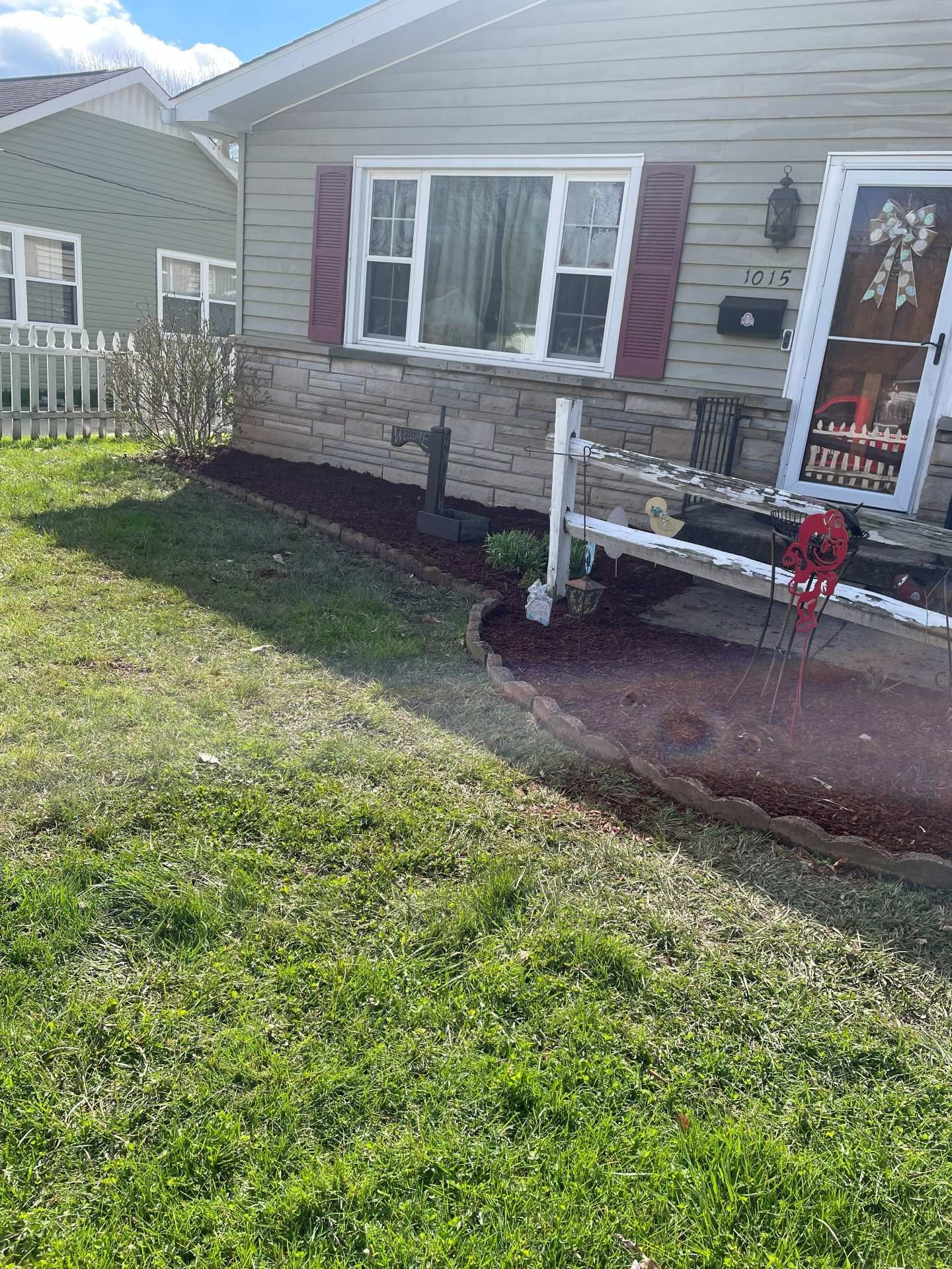 Front yard of a beige house with a small porch, windows, and a grassy lawn in sunlight
