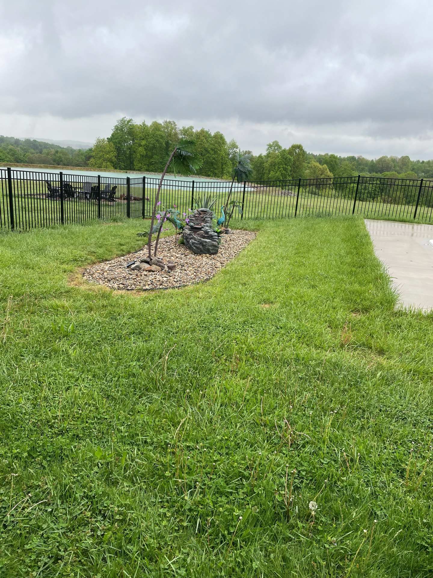 Grassy park with a small sculpture display on a gravel bed beside a paved path under cloudy skies