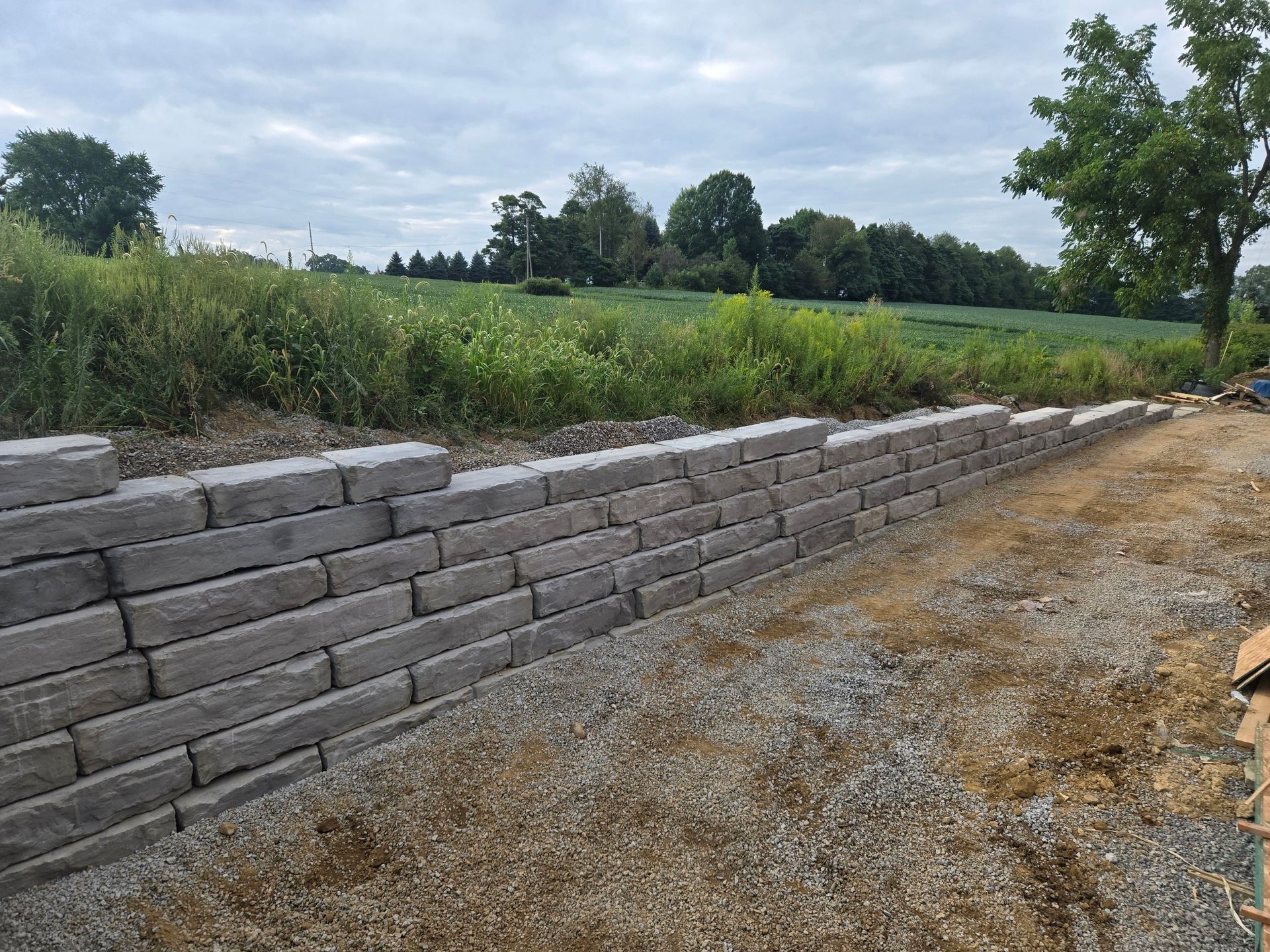 Gray stone retaining wall along a gravel path, with a grassy field in the background.