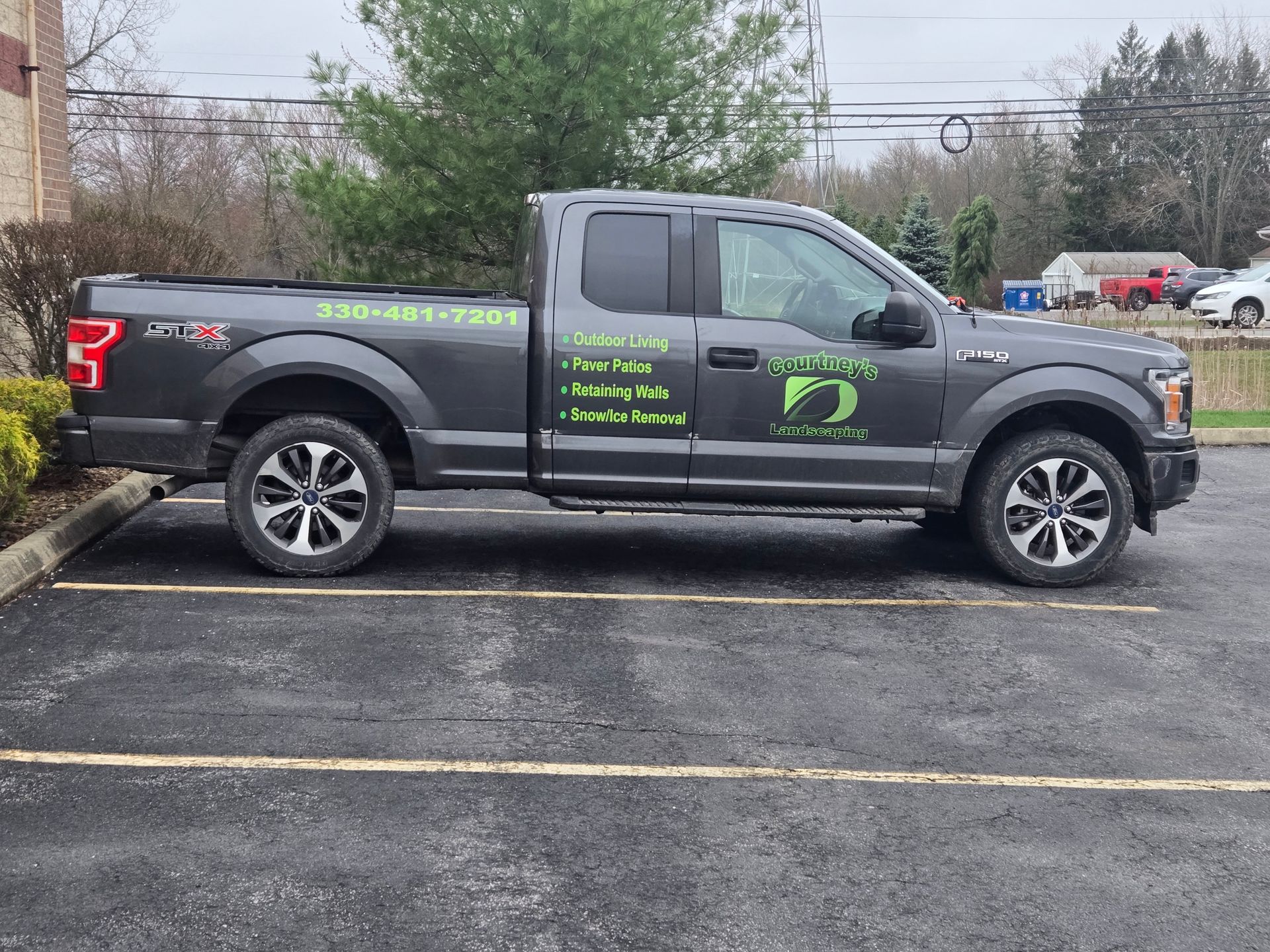 Gray pickup truck parked on asphalt, advertising lawn care services, with a phone number visible.