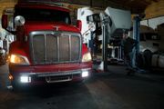 Red semi-truck in a repair shop with a mechanic. The truck is under a lift.