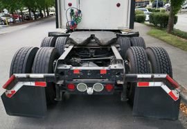 Rear view of a semi-truck chassis and wheels parked on a street; mud flaps with reflective tape.