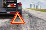 Orange warning triangle on a road, trailer in background near grain silos.
