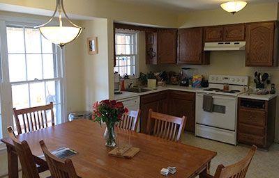 A kitchen with a table and chairs and a vase of flowers on the table.