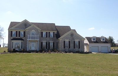 A large house with two garages is sitting in the middle of a grassy field.
