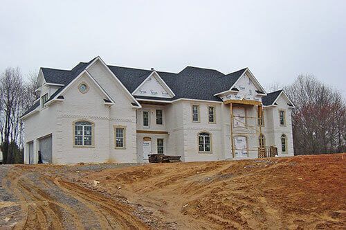 A large white house is being built on top of a dirt hill.