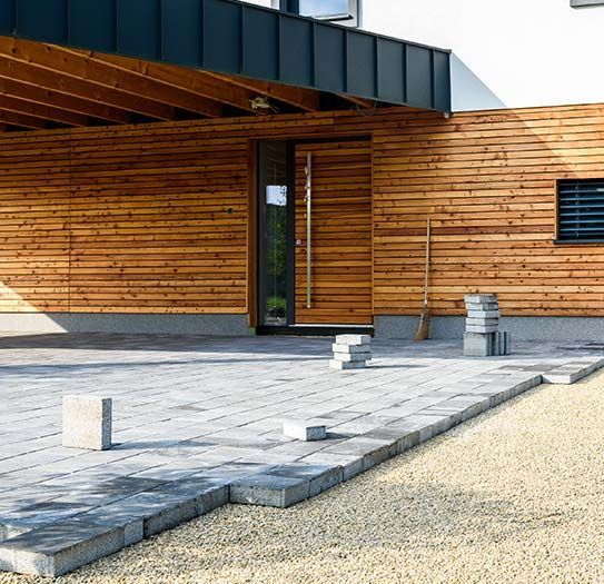 A house with a wooden facade and a brick driveway in front of it.