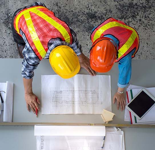 Two construction workers are looking at a blueprint on a table.