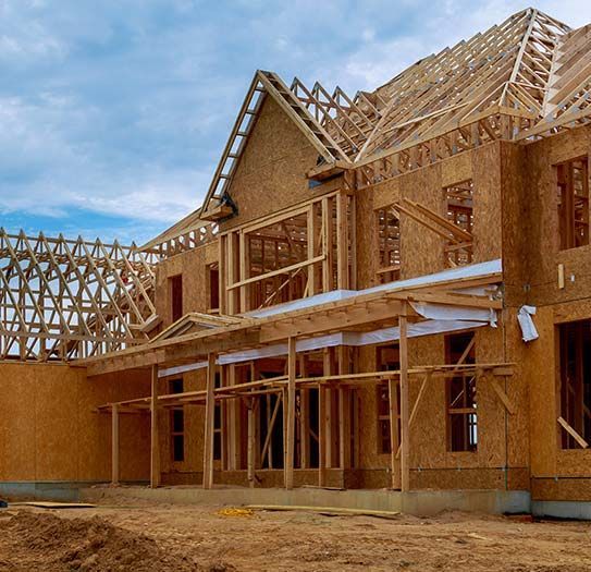 A large wooden house is being built with a blue sky in the background