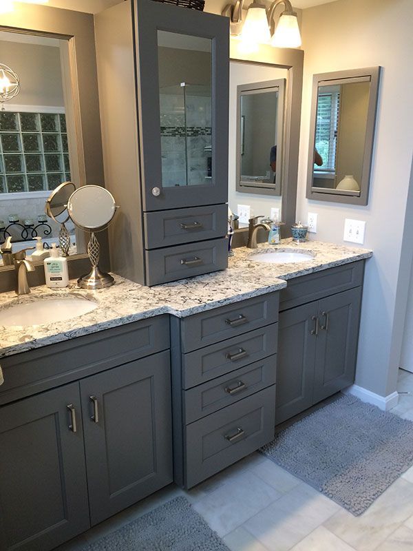 A bathroom with two sinks , two mirrors , and gray cabinets.