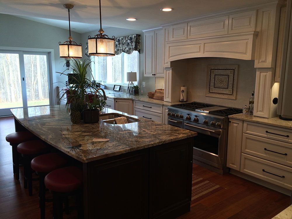 A kitchen with white cabinets , granite counter tops , stainless steel appliances and a large island.